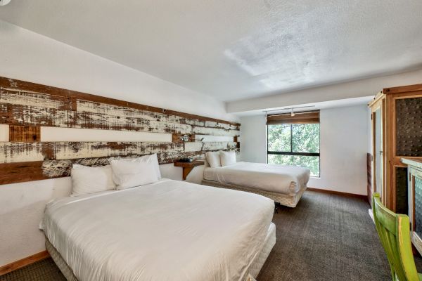 A hotel room with two beds, decorative headboard, a window, and some furniture including a chair and a wooden cabinet.
