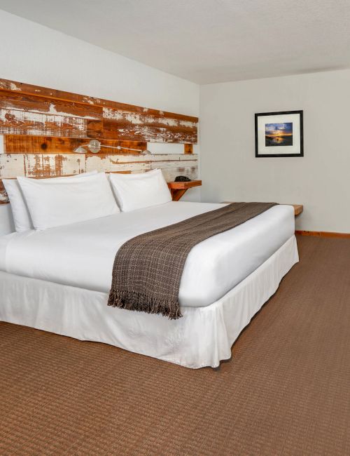 A clean hotel room with a king-sized bed, wooden headboard, desk, chair, wall-mounted TV, and framed picture on the wall above the bed ending the sentence.