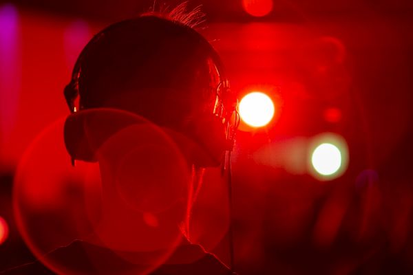A person wearing headphones is shown from the back, bathed in red lighting, with blurred bright lights in the background.