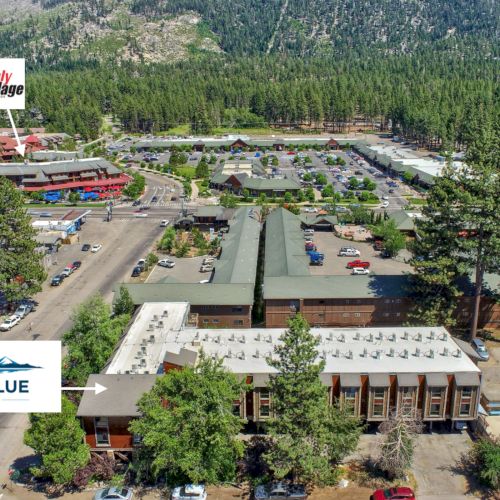 An aerial view of the Tahoe Blue Hotel and surrounding buildings, nestled in a mountainous forest area with ample parking and nearby attractions.